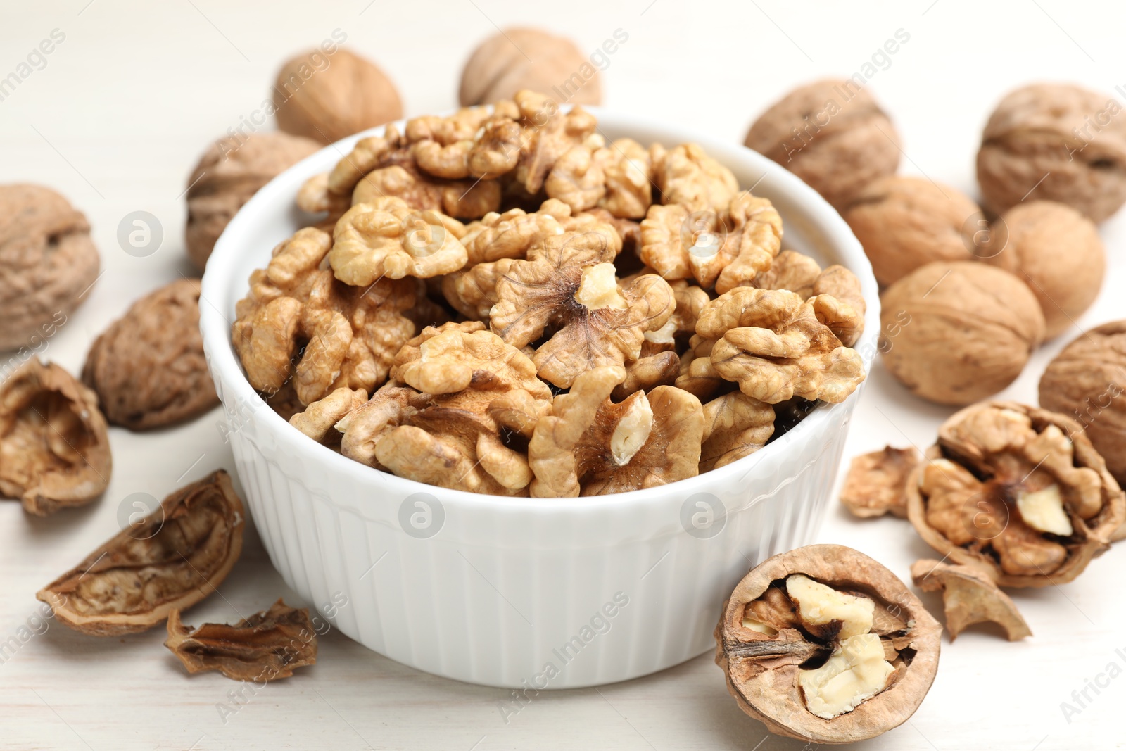 Photo of Peeled walnuts in bowl and whole ones on light table, closeup