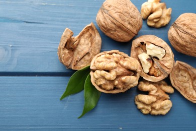 Photo of Fresh walnuts with shells and green leaves on blue wooden table, flat lay. Space for text