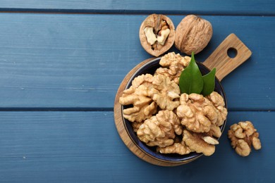 Photo of Fresh walnuts and green leaves in bowl on blue wooden table, flat lay. Space for text