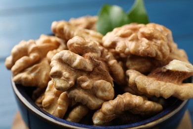 Photo of Fresh walnuts in bowl on blue table, closeup