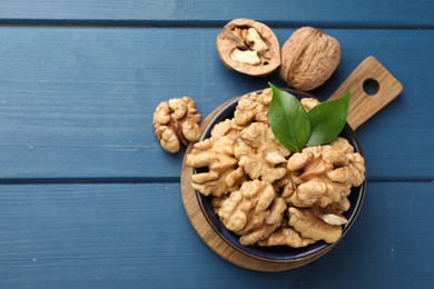 Photo of Fresh walnuts and green leaves in bowl on blue wooden table, flat lay. Space for text