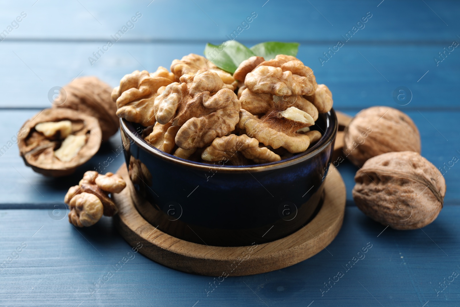 Photo of Fresh walnuts in bowl on blue wooden table, closeup