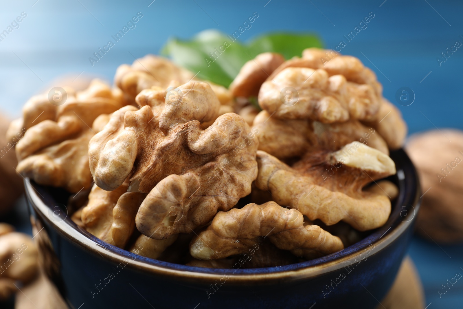 Photo of Fresh walnuts in bowl on blue table, closeup