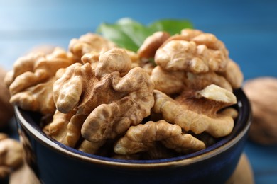 Photo of Fresh walnuts in bowl on blue table, closeup