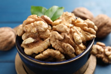 Photo of Fresh walnuts in bowl on blue table, closeup