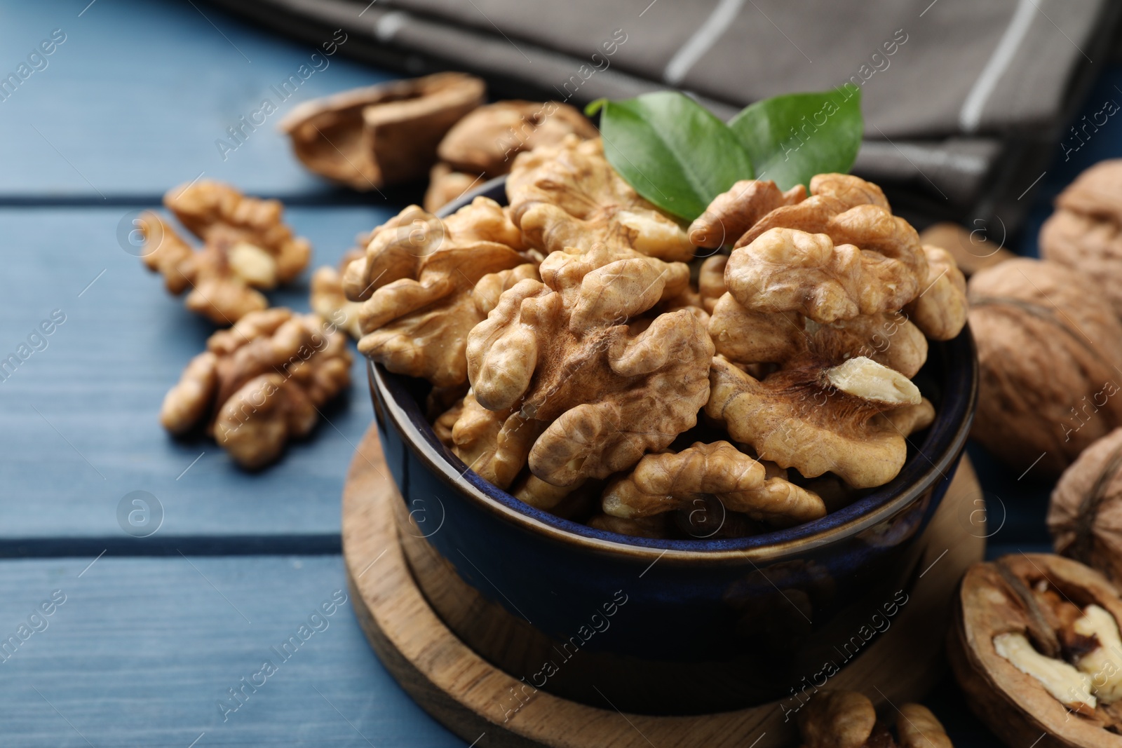 Photo of Fresh walnuts and green leaves in bowl on blue wooden table, closeup. Space for text