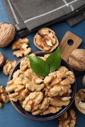 Photo of Fresh walnuts and green leaves in bowl on blue wooden table, flat lay