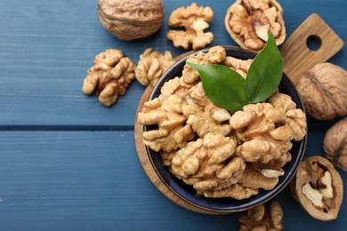 Photo of Fresh walnuts and green leaves in bowl on blue wooden table, flat lay. Space for text