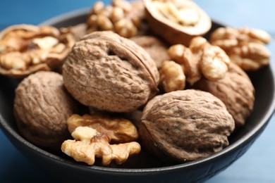 Photo of Fresh walnuts in bowl on blue table, closeup