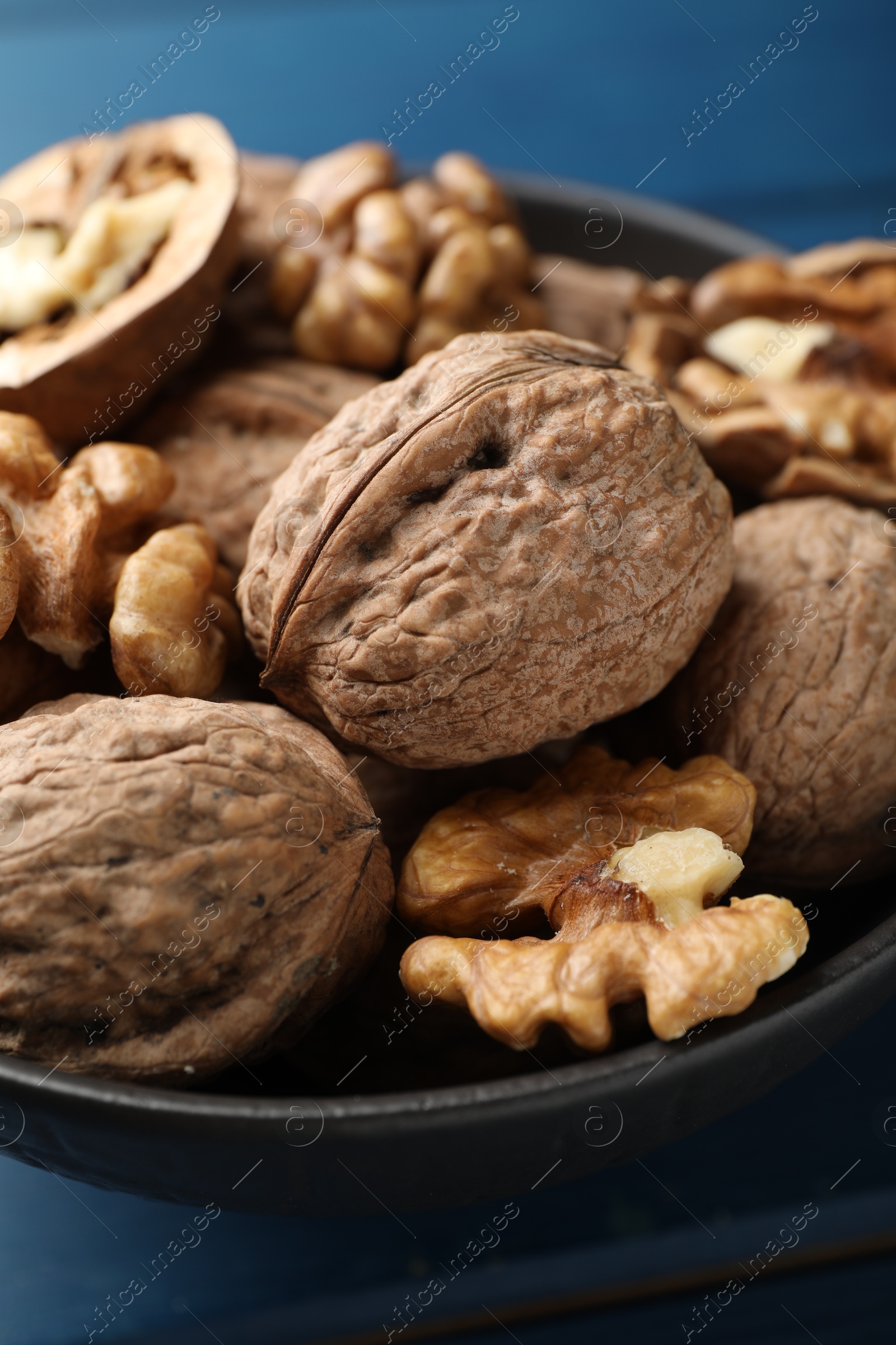 Photo of Fresh walnuts in bowl on blue table, closeup