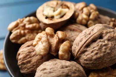 Photo of Fresh walnuts in bowl on blue table, closeup