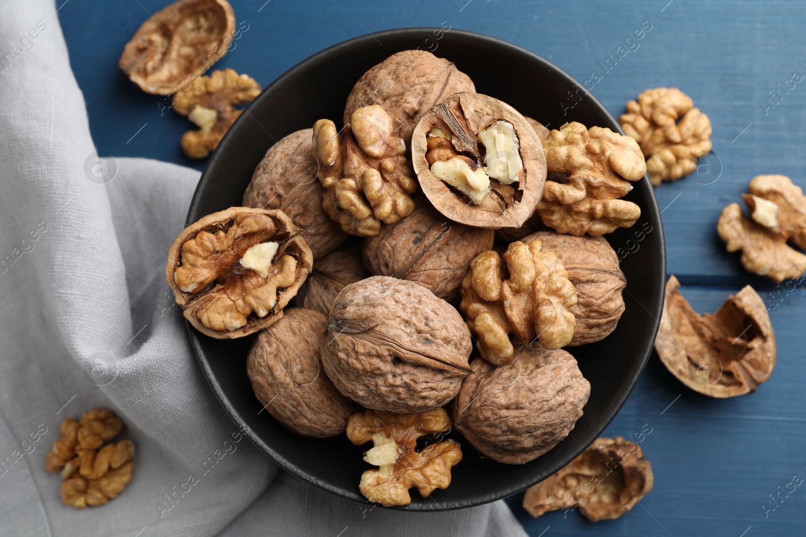 Photo of Fresh walnuts in bowl on blue wooden table, flat lay