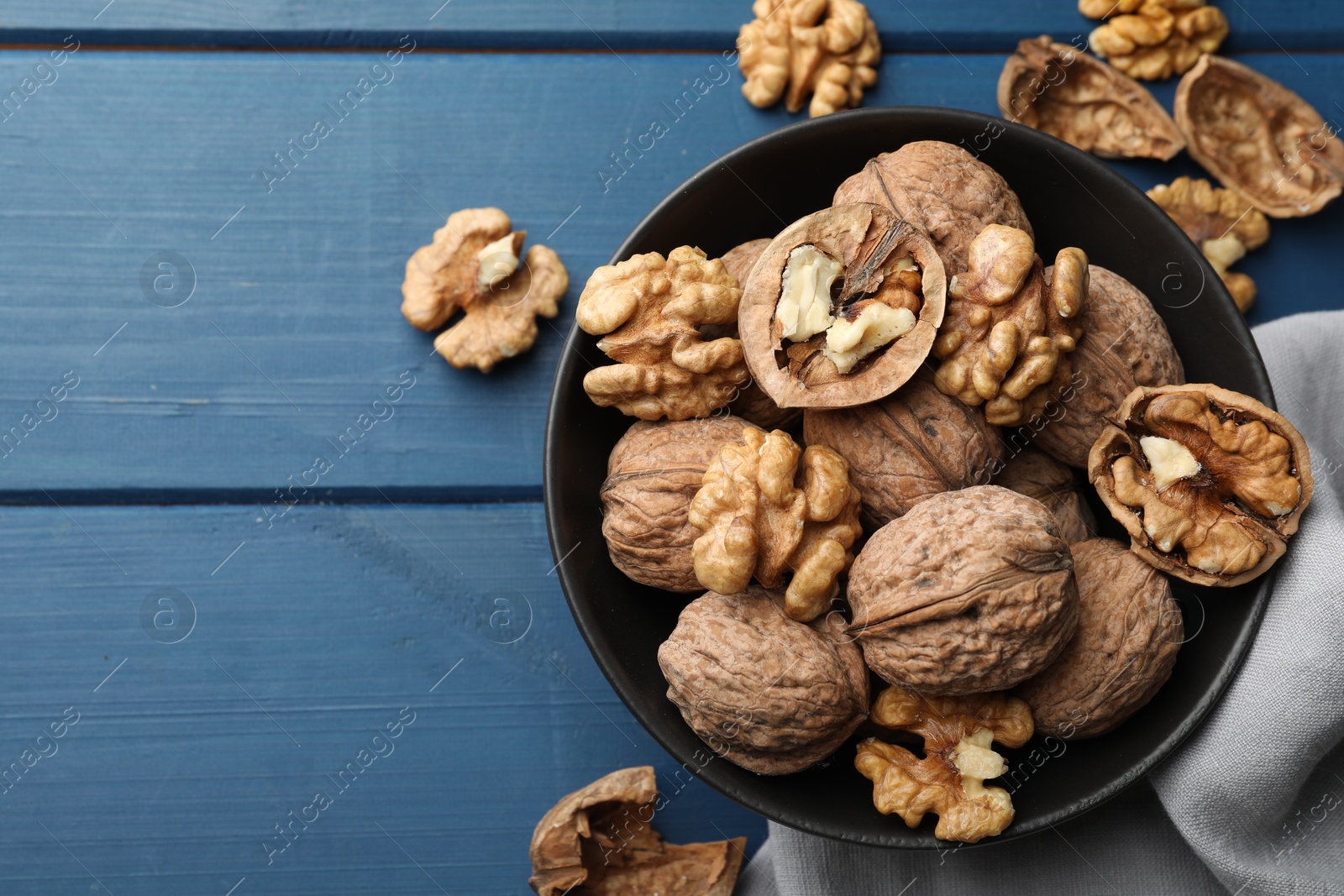 Photo of Fresh walnuts in bowl on blue wooden table, flat lay. Space for text