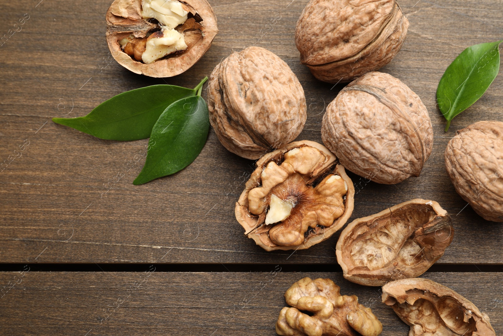 Photo of Fresh walnuts and green leaves on wooden table, flat lay. Space for text