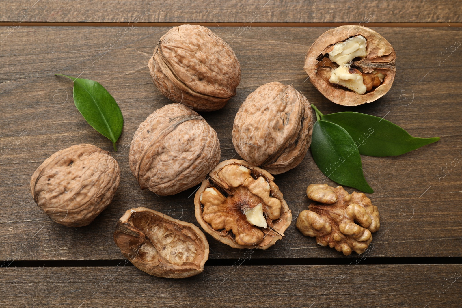 Photo of Fresh walnuts and green leaves on wooden table, flat lay