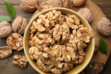 Photo of Peeled walnuts in bowl and whole ones on table, flat lay