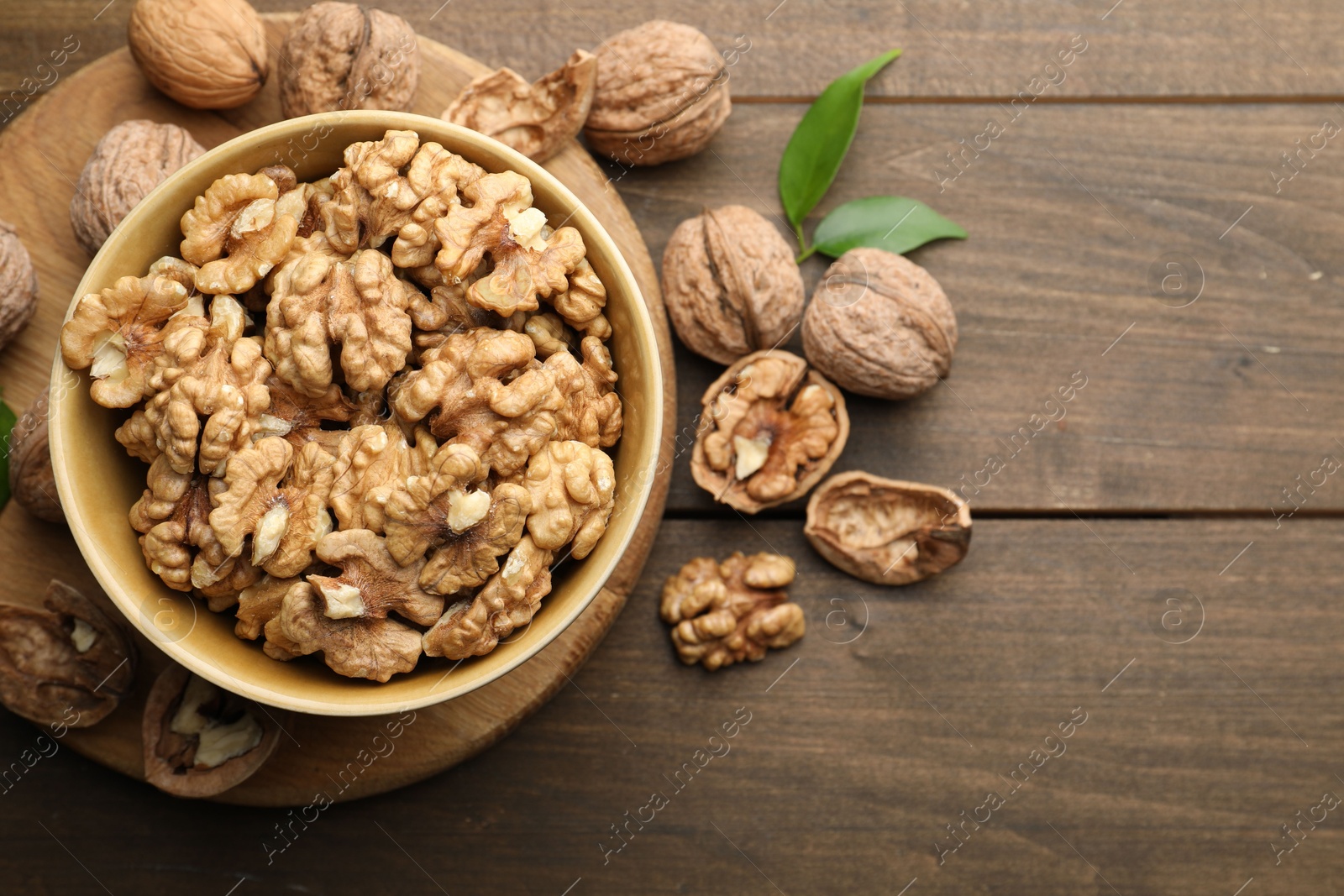 Photo of Peeled walnuts in bowl and whole ones on wooden table, flat lay. Space for text