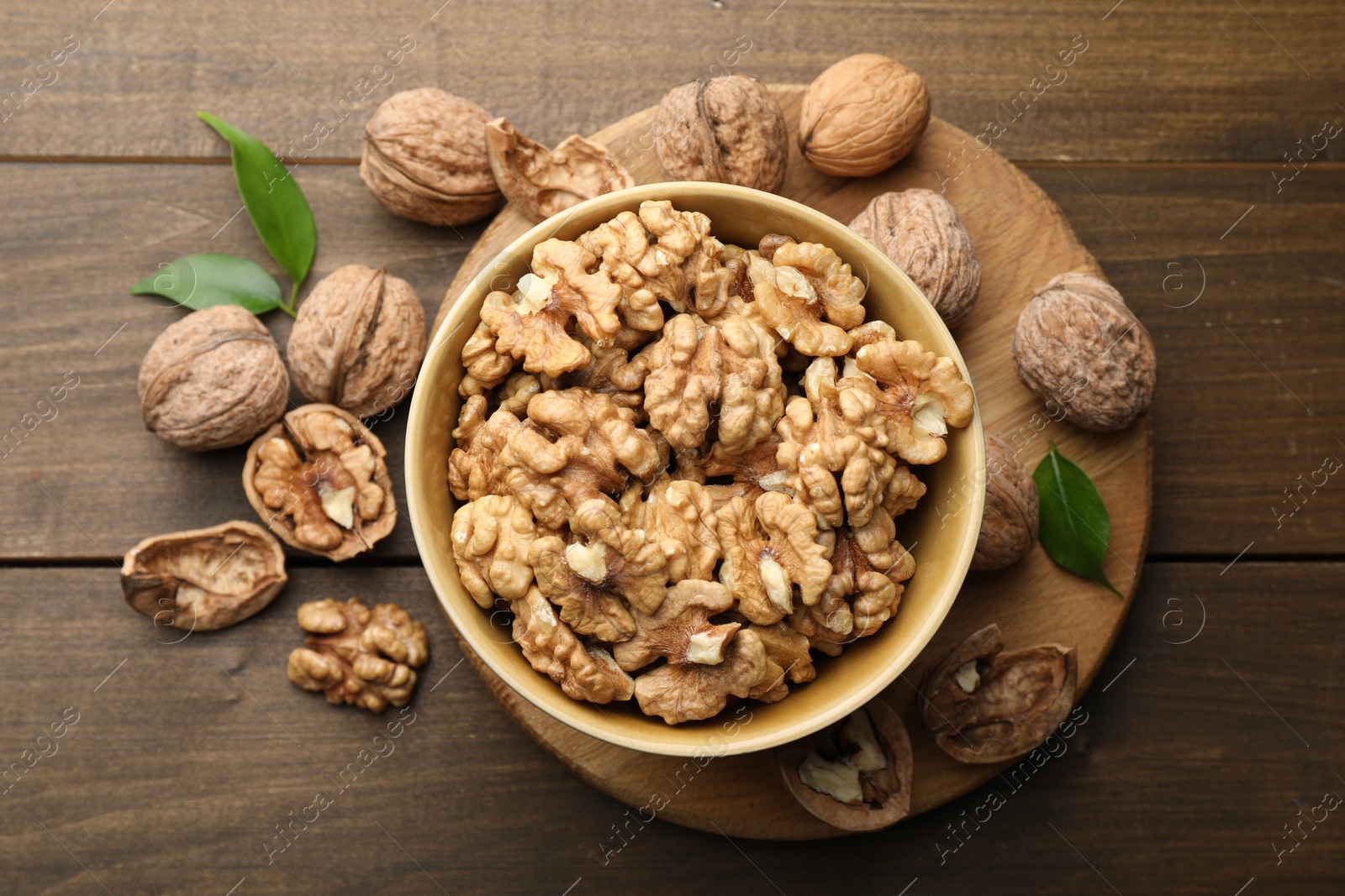 Photo of Peeled walnuts in bowl and whole ones on wooden table, flat lay