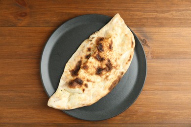 Photo of Plate with tasty calzone on wooden table, top view