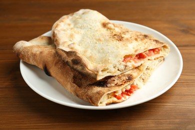 Photo of Halves of tasty calzone with meat, cheese and tomato on wooden table, closeup