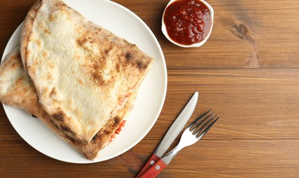 Photo of Halves of tasty calzone served with sauce on wooden table, flat lay. Space for text