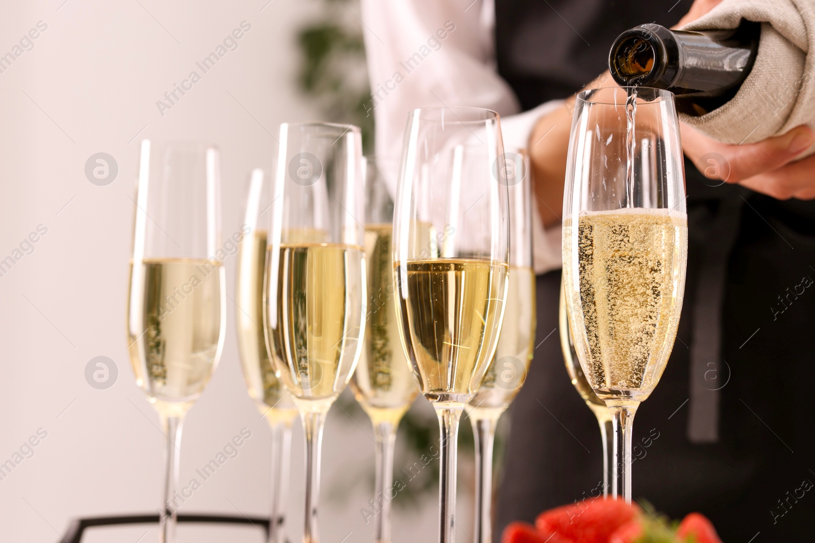 Photo of Waiter filling glasses with champagne indoors, closeup