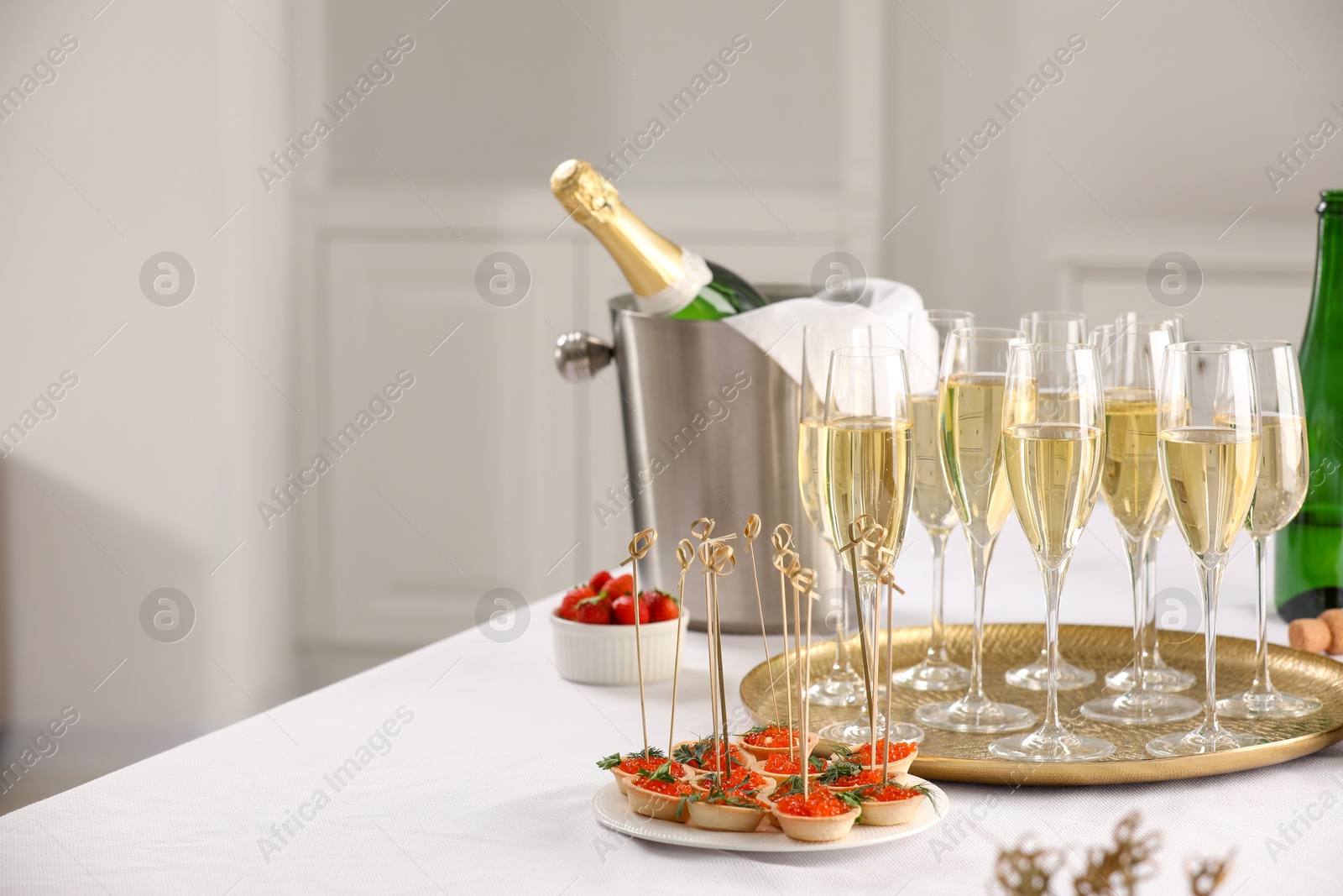 Photo of Champagne, strawberries and canapes with red caviar on white table. Space for text