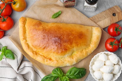 Photo of Tasty vegetarian calzone with tomatoes, mozzarella cheese and basil on grey table, top view