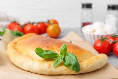 Photo of Tasty vegetarian calzone with basil and tomatoes on table, closeup