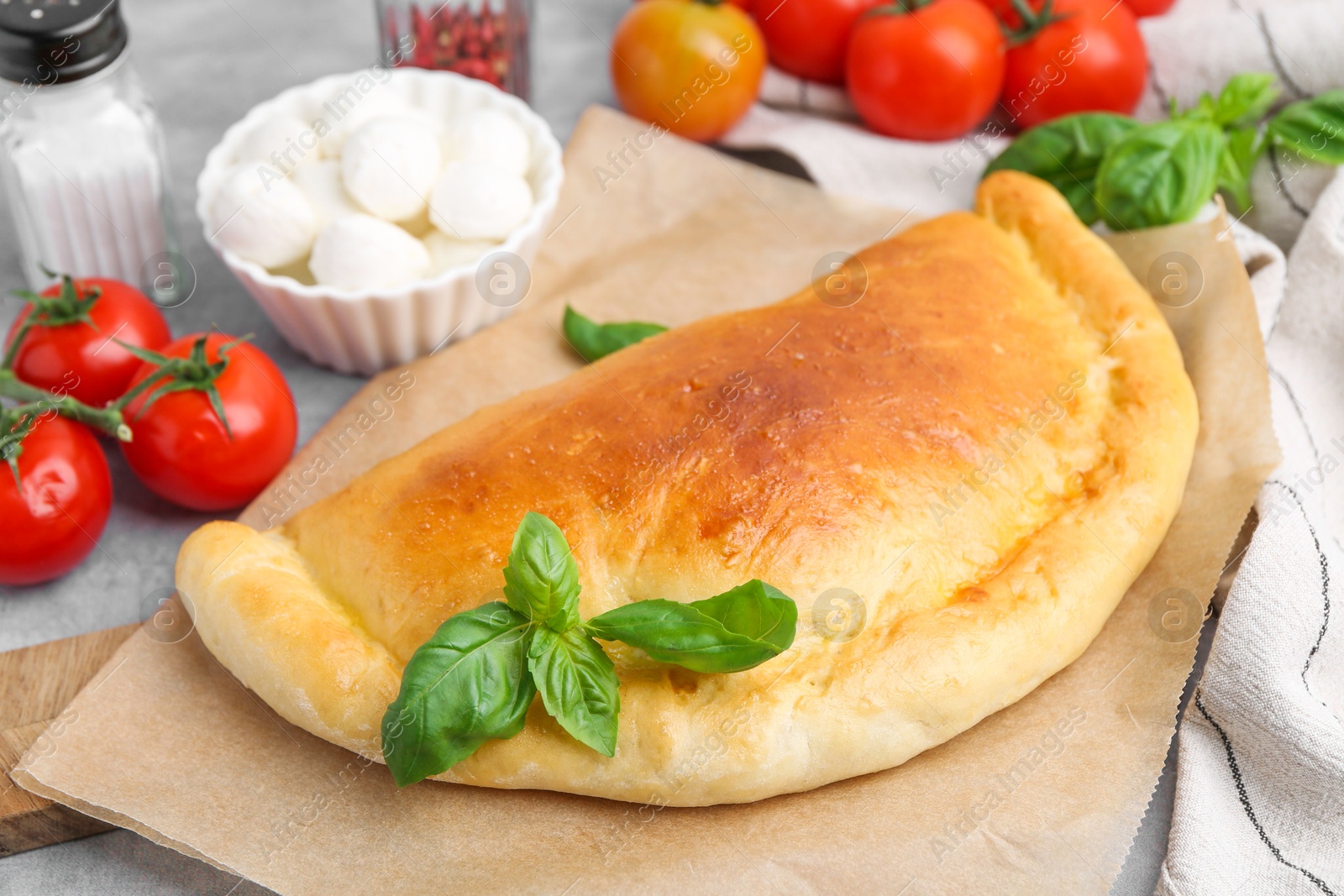 Photo of Tasty vegetarian calzone with tomatoes, mozzarella cheese and basil on grey table, closeup