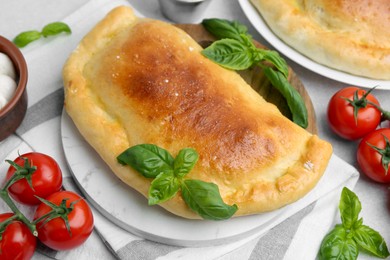 Photo of Tasty vegetarian calzone with basil and tomatoes on table, closeup