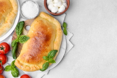 Photo of Tasty vegetarian calzone with basil, tomatoes and mozzarella cheese on light table, flat lay. Space for text