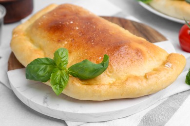 Photo of Tasty vegetarian calzone with basil on light table, closeup