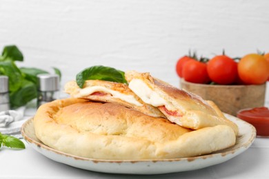 Photo of Pieces of delicious calzone pizza with mozzarella, tomatoes and basil on white table, closeup