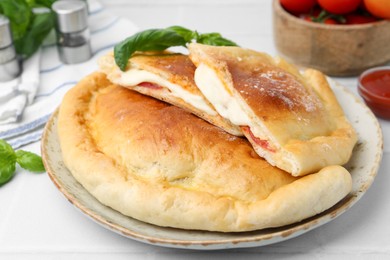 Photo of Pieces of delicious calzone pizza with mozzarella, tomatoes and basil on white table, closeup