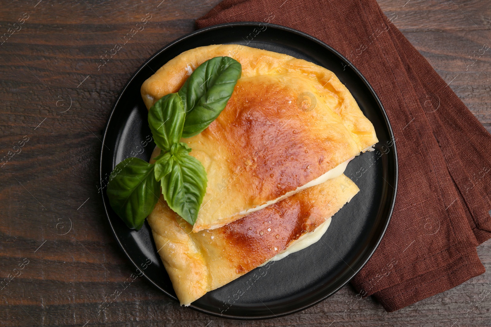 Photo of Pieces of delicious calzone pizza with mozzarella, tomatoes and basil on wooden table, top view