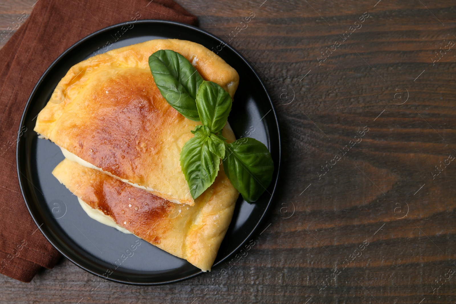 Photo of Pieces of delicious calzone pizza with mozzarella, tomatoes and basil on wooden table, top view. Space for text