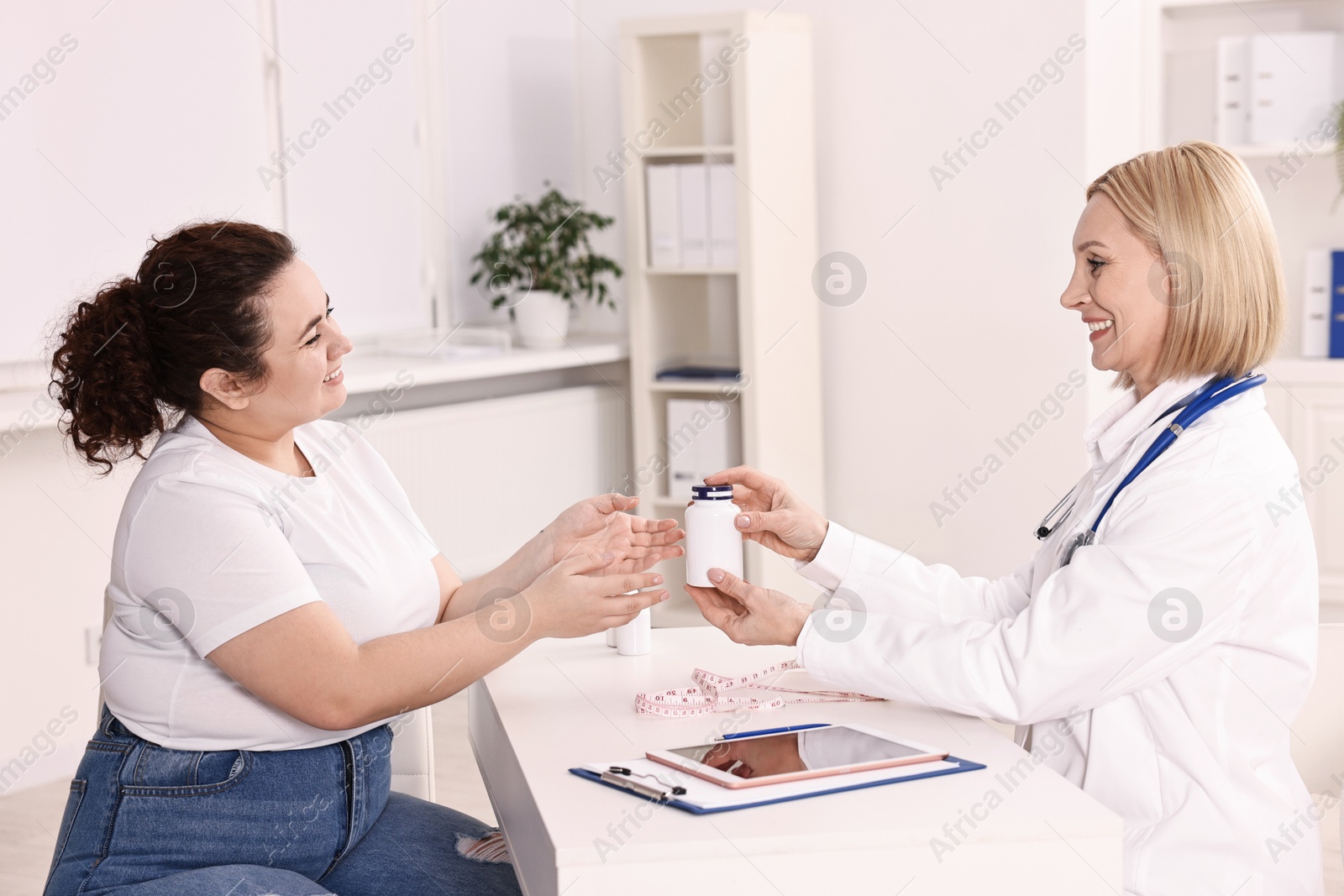 Photo of Weight loss. Smiling nutritionist giving medical bottle with pills to patient at table in clinic