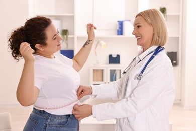 Photo of Happy woman lost weight. Smiling nutritionist measuring patient's waist with tape in clinic