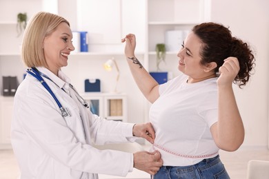 Photo of Happy woman lost weight. Smiling nutritionist measuring patient's waist with tape in clinic