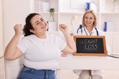 Photo of Happy woman lost weight and nutritionist with small blackboard in clinic