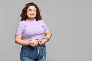 Photo of Happy plus size woman measuring waist with tape and holding pile of weight loss supplements on grey background. Space for text