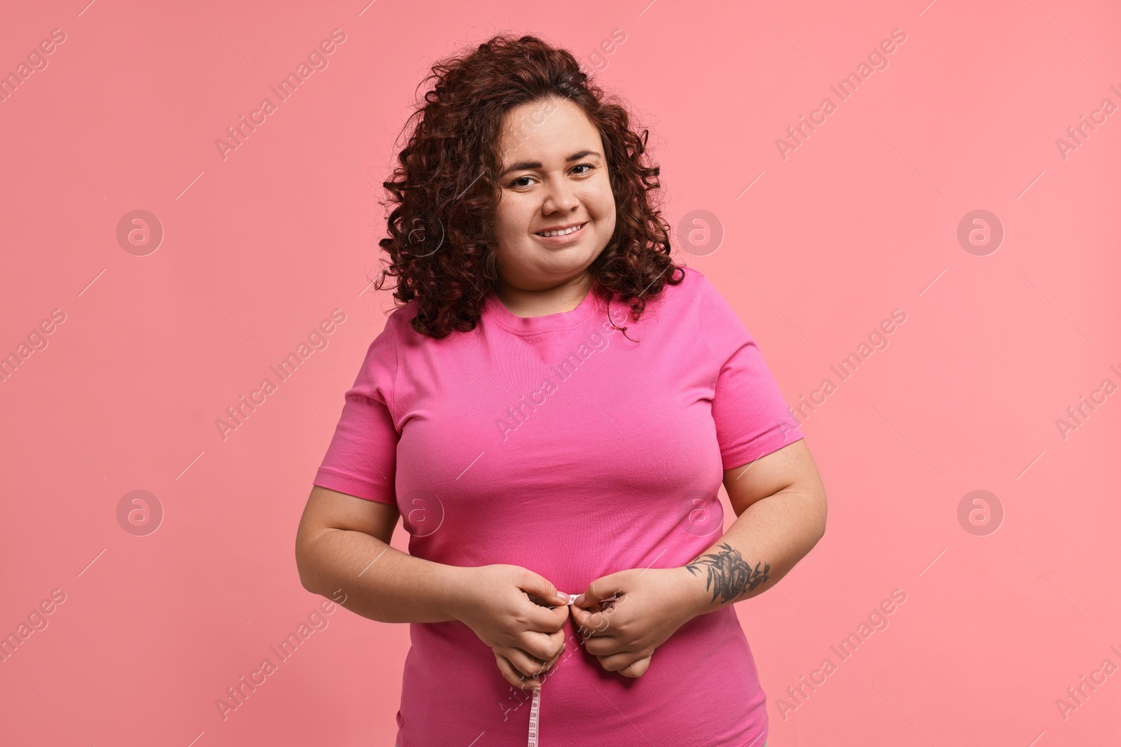 Photo of Weight loss. Happy plus size woman measuring waist with tape on pink background