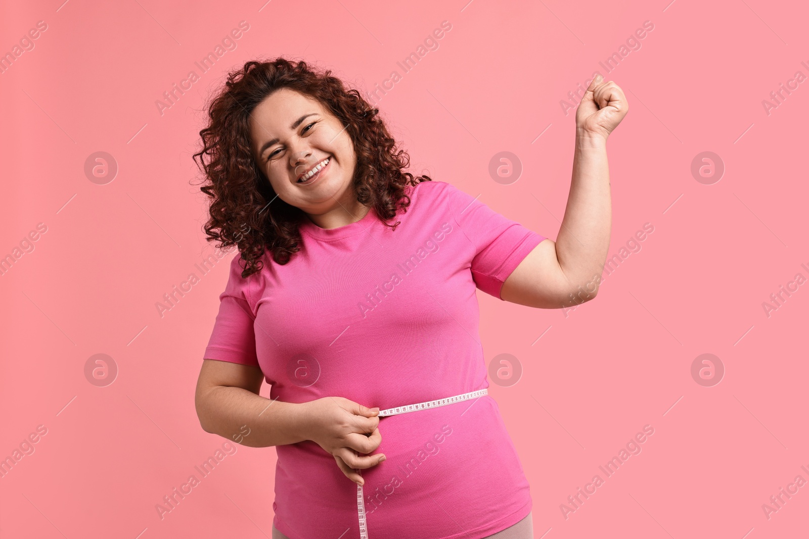 Photo of Weight loss. Happy plus size woman measuring waist with tape on pink background