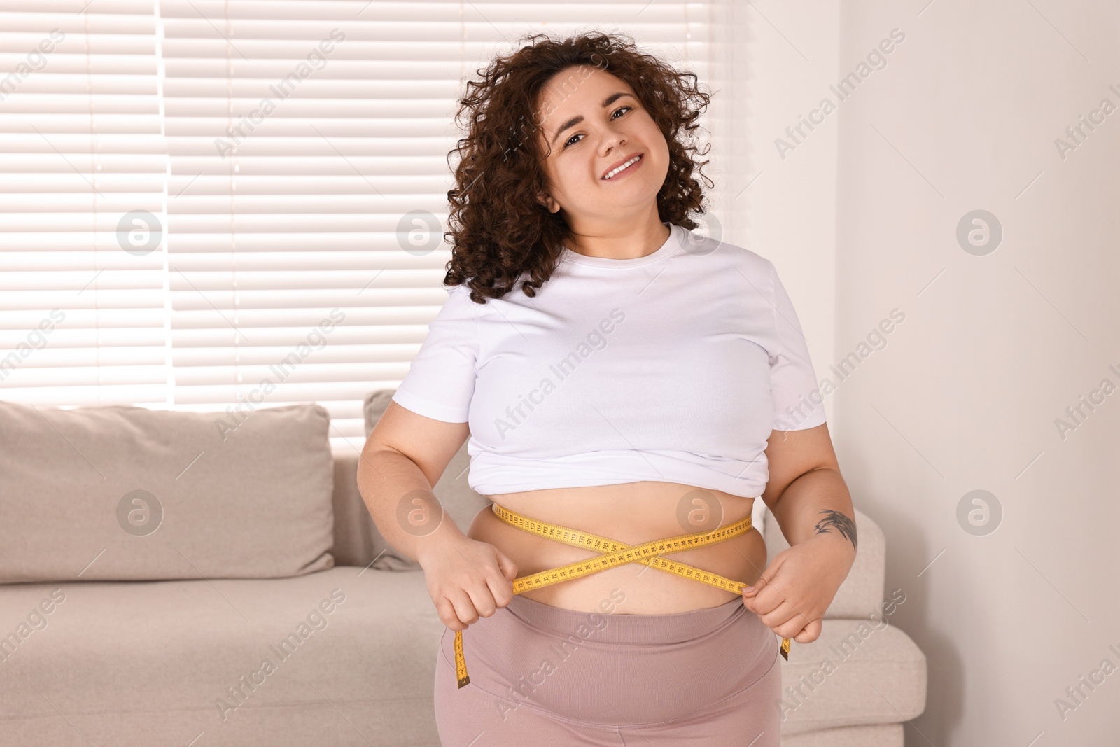 Photo of Weight loss. Happy plus size woman measuring waist with tape at home. Space for text