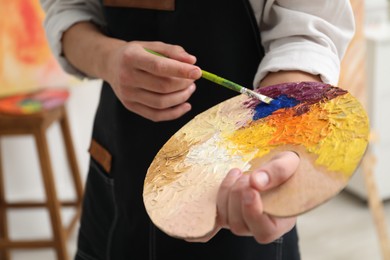 Man with palette and paintbrush indoors, closeup