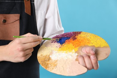 Photo of Man with palette and paintbrush on light blue background, closeup