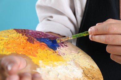 Photo of Man with palette and paintbrush on light blue background, closeup