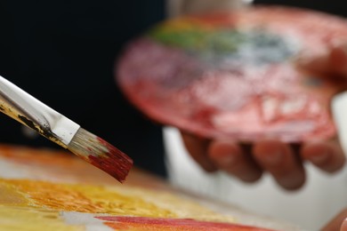 Photo of Man with palette and paintbrush drawing picture indoors, selective focus