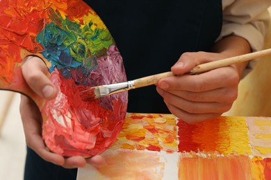 Photo of Man with palette and paintbrush drawing picture indoors, closeup